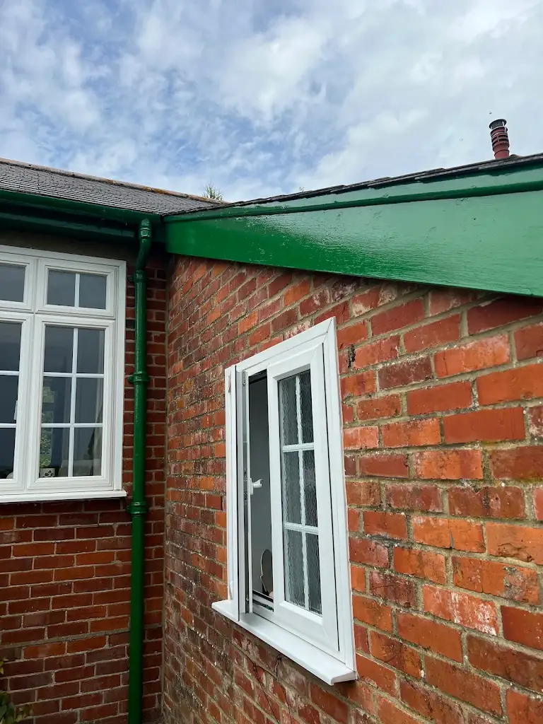 Brick house exterior painting with white trims and green roofline, professional work